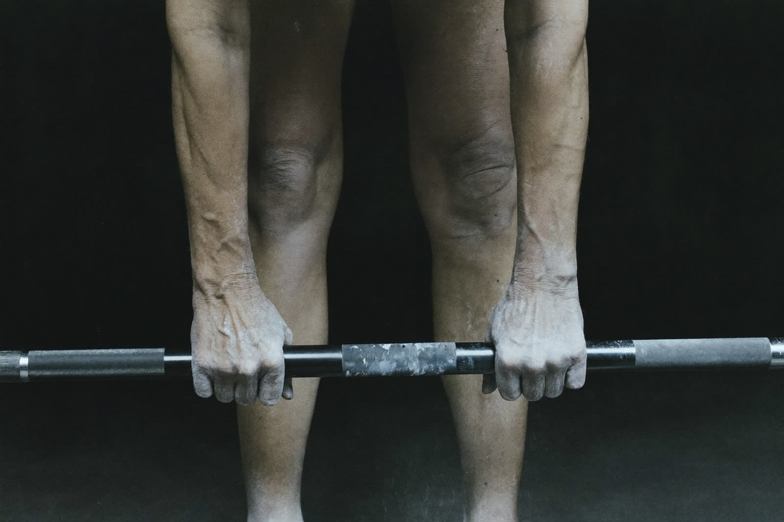 Chalked hands gripping a barbell at the start of a deadlift